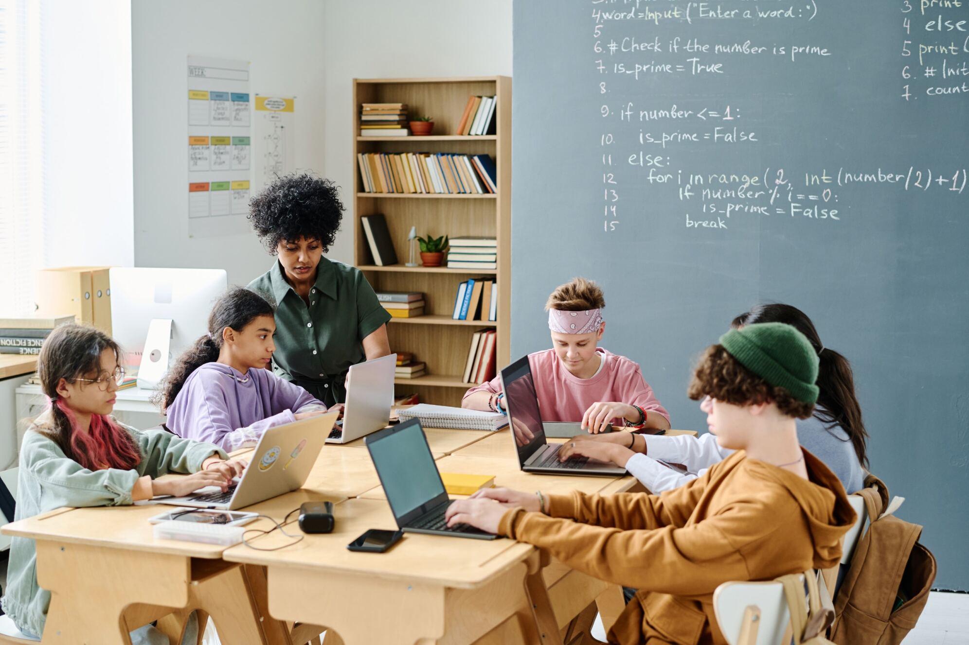 Kids and teens sitting around a table in front of their laptops with their instructor and learning programming on an advanced level.