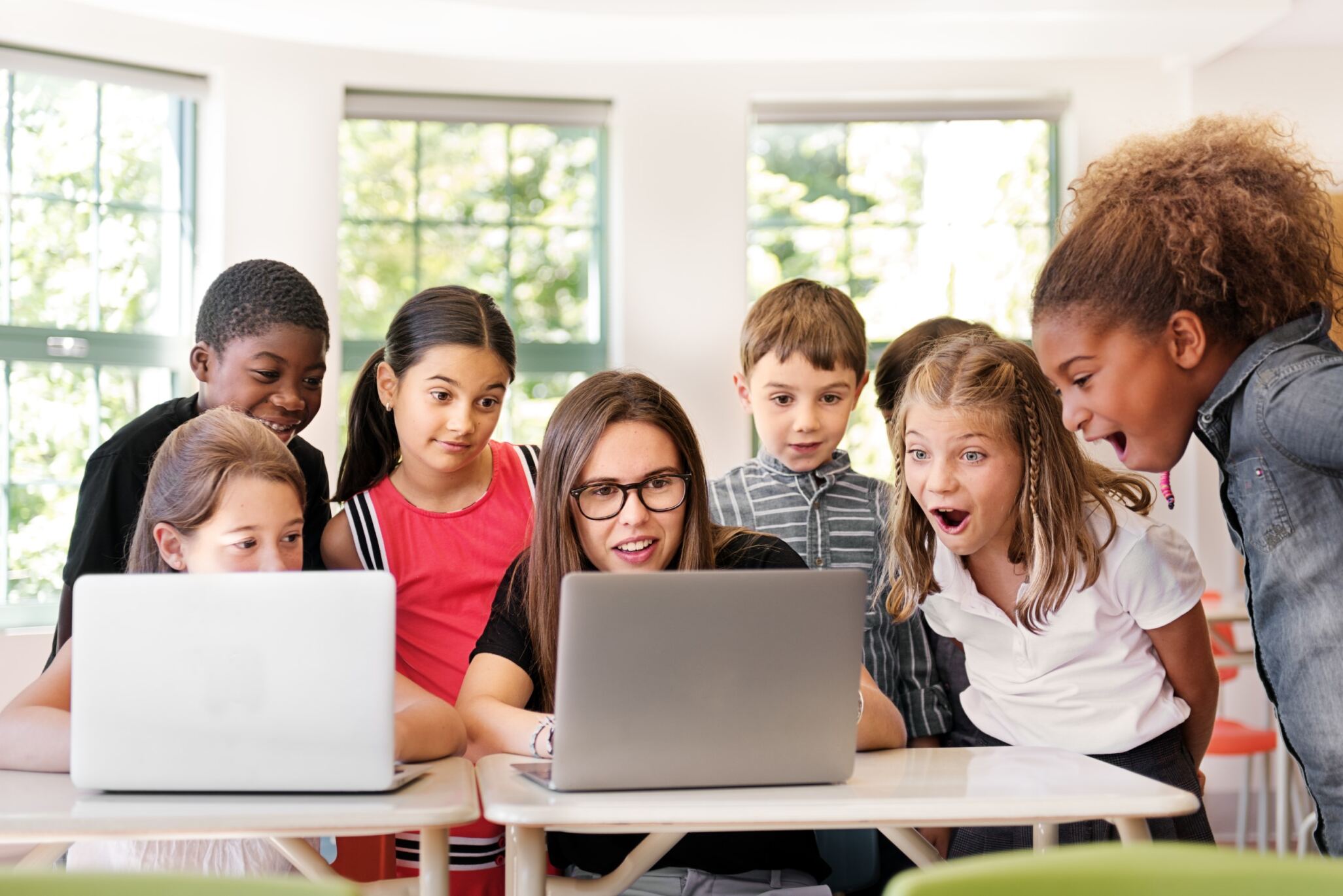 Children during a company visit standing around a woman and her laptop and watching what she is doing.