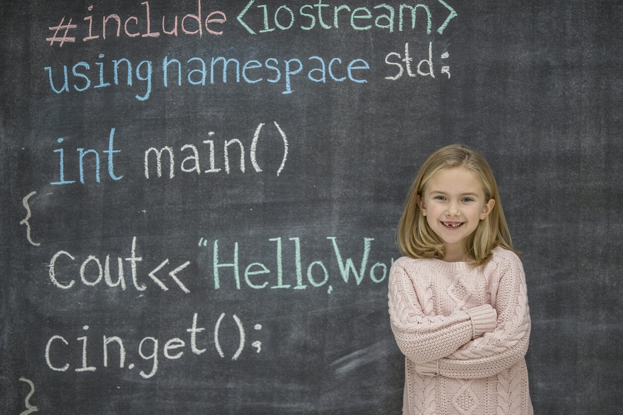 Girl standing in front of a blackboard with codes written all over it after a programming class for kids with Berlitz Digital School.