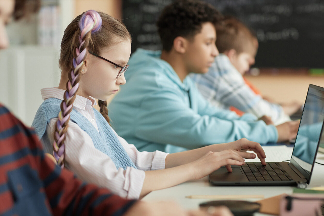 Girl with locks and glasses in front of a computer learning about front-end development for kids with Berlitz Digital School.