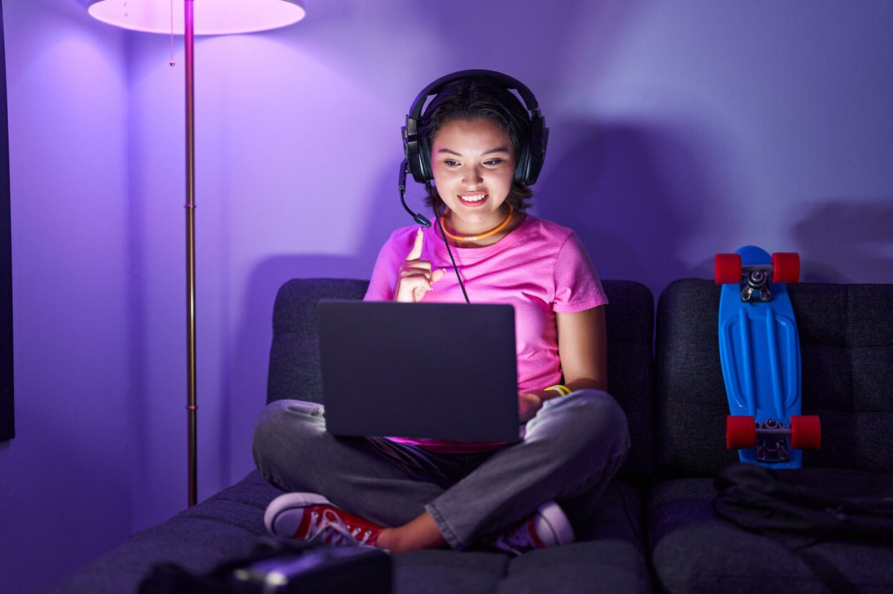 A girl with headphones sitting on a couch and learning programming for kids with Berlitz Digital School online on her laptop.