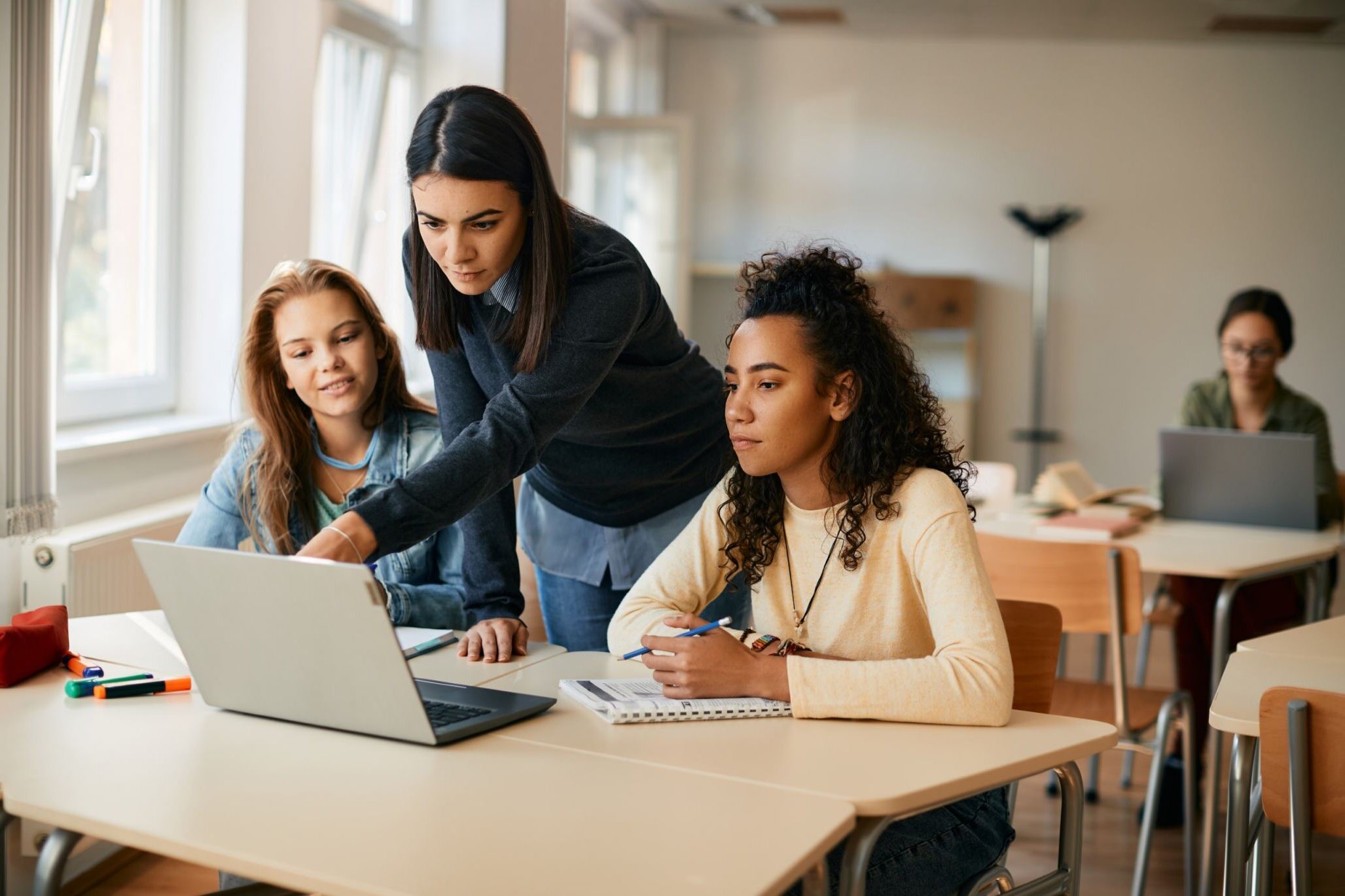 Instructor showing two girls how they can develop applications on an advanced level on a laptop.