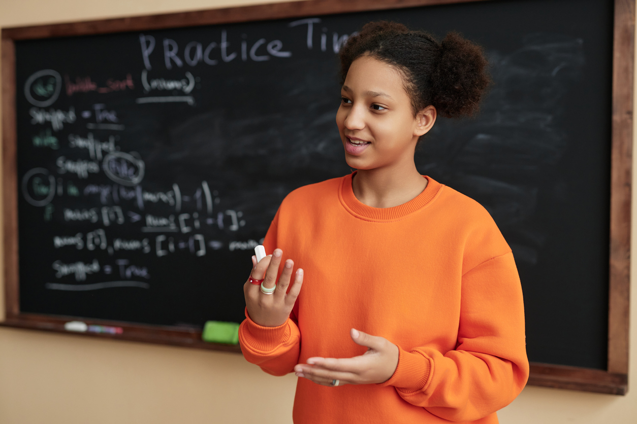 Teenage girl answering by blackboard in school classroom