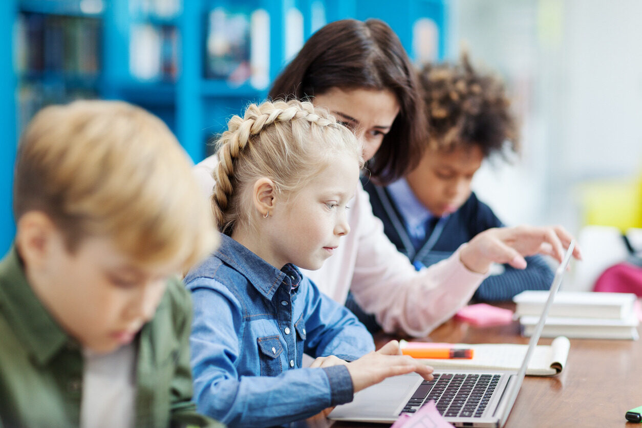 Teacher and students talking while watching a laptop screen during a programming class.