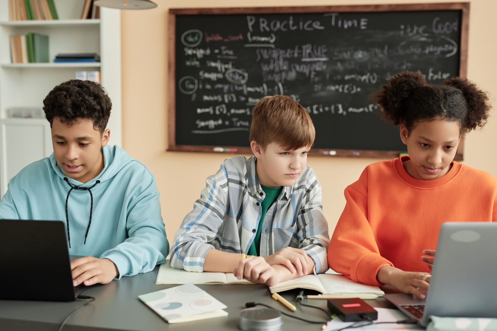 Students with laptops and notebooks learning about back-end development together during a programming class for kids with Berlitz Digital School.