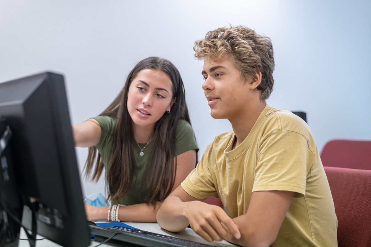 Student pointing at a monitor and showing it to another students during their advanced application development class for kids and teens with Berlitz Digital School