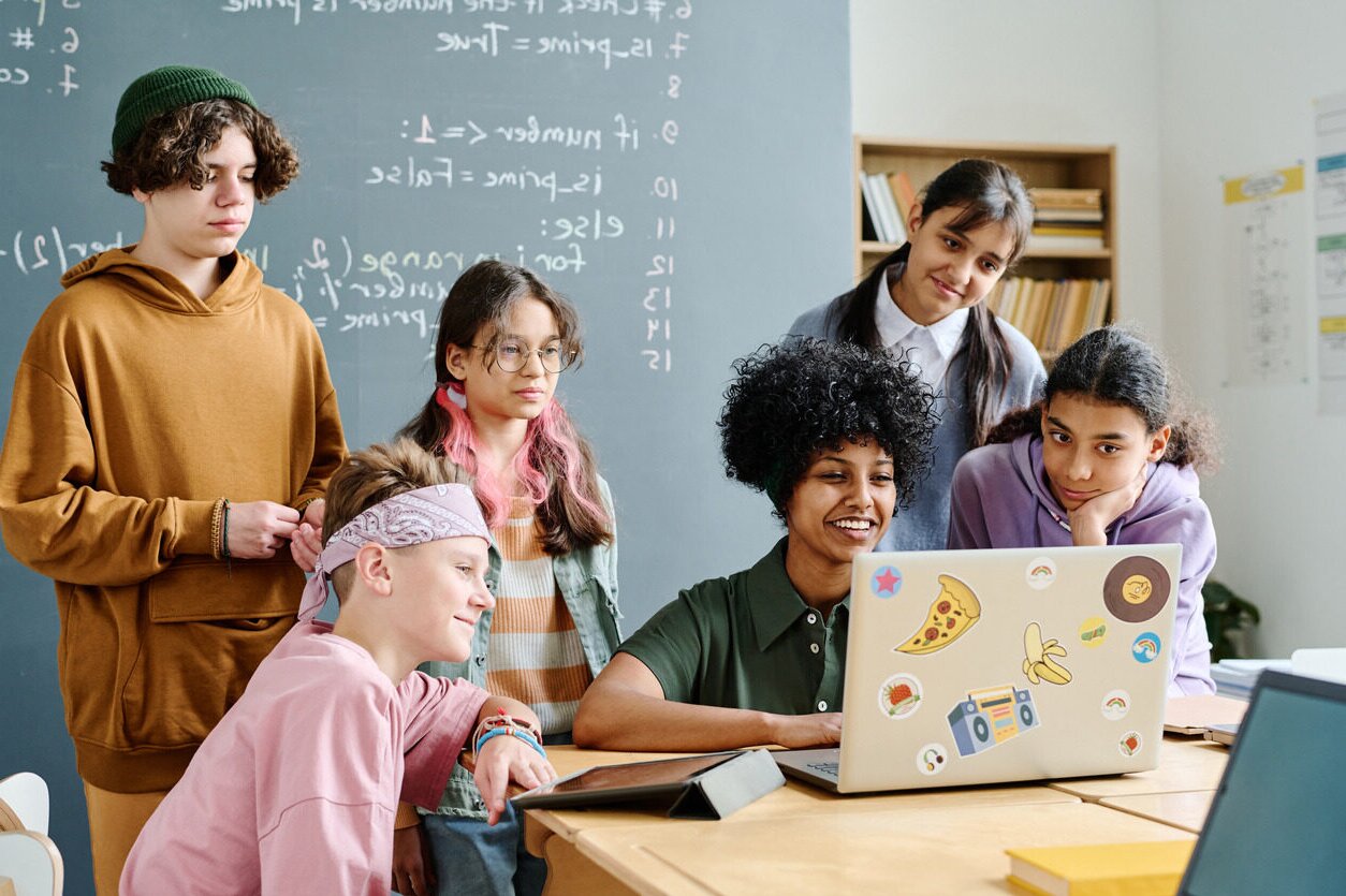 A group of students in front of a computer learning how to code with their instructor in an in-person programming course for children with Berlitz Digital School.