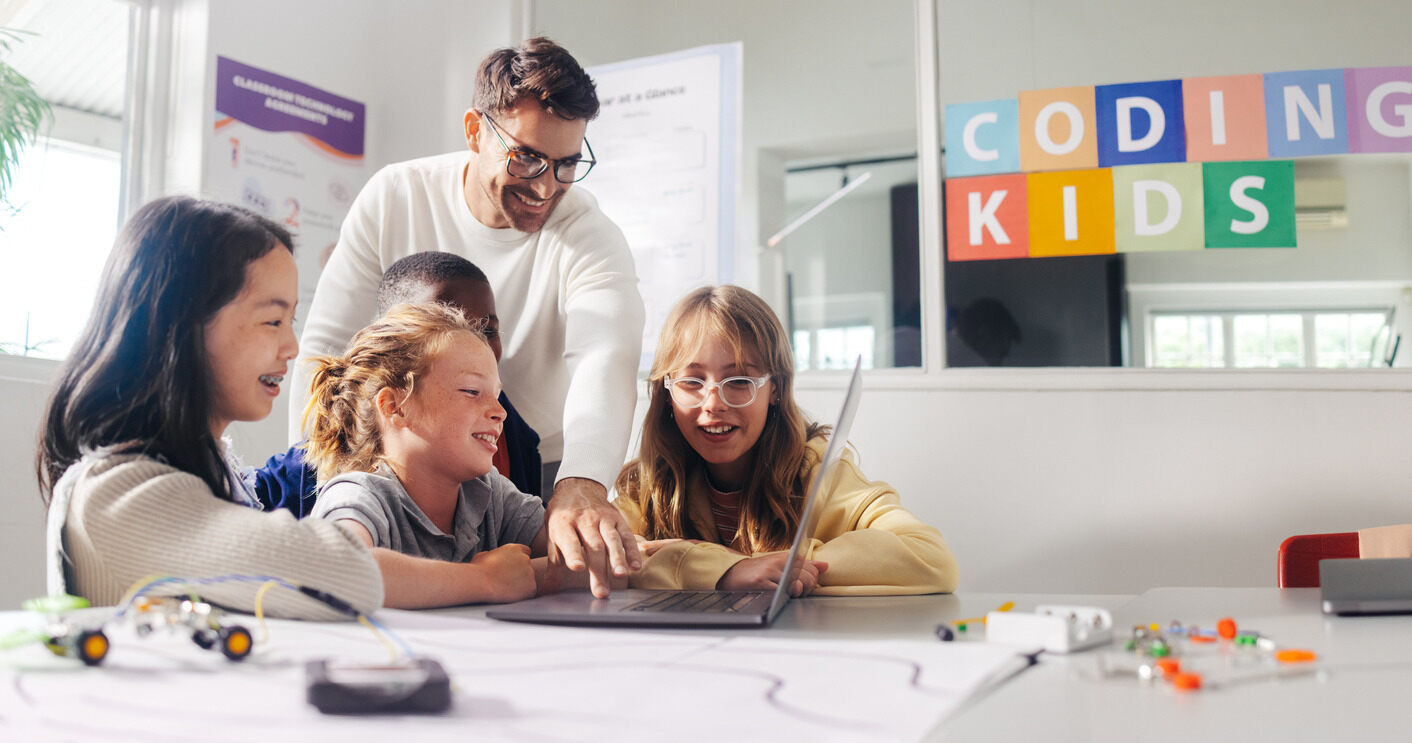 Students and their teacher in front of the laptop discussing the basics of programming.