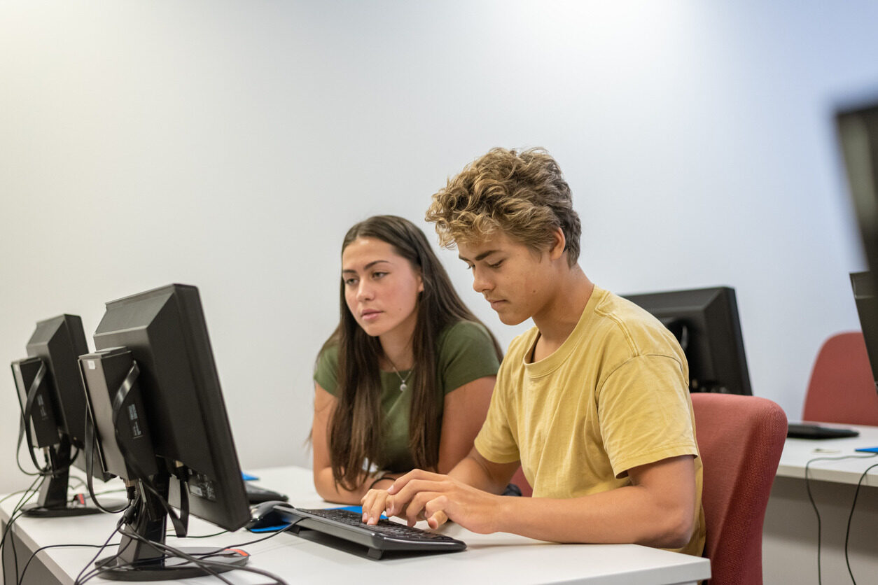 Teens watching a computer screen together and typing on a keyboard during Summer School.